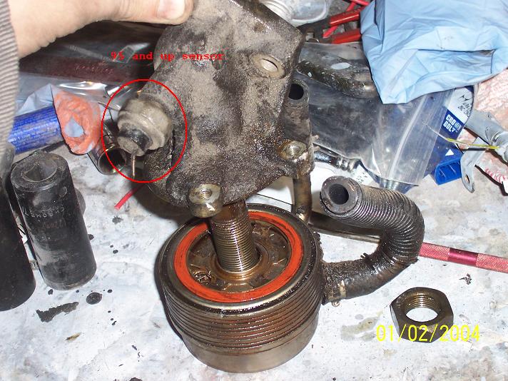 Dirty oil cooler assembly with red gasket and ribbed hose, held by a hand