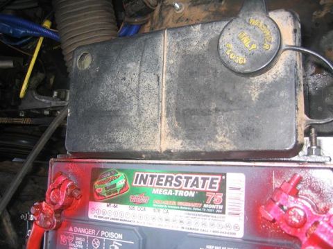 1986 Ford Bronco - Close-up of a vehicle's engine bay, focusing on the battery and a protective cover.