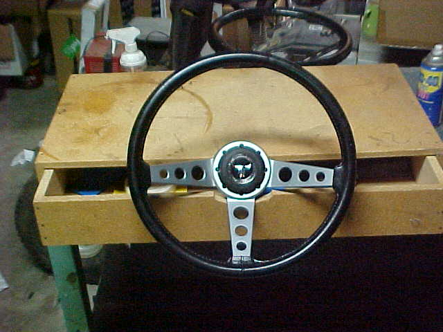 Three-spoke drilled-aluminum steering wheel with black rim propped on a workbench