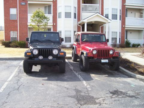 1998 Jeep TJ - Two Jeep Wranglers are parked side-by-side in a parking lot in front of a brick apartment building.
