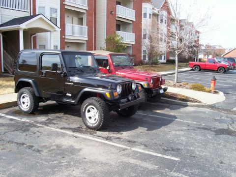 1998 Jeep TJ - Two Jeep Wranglers, one black and one red, are parked side-by-side in an apartment complex parking lot.