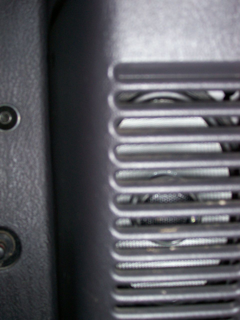 Close-up of a vehicle's interior speaker grille with a textured panel to the left