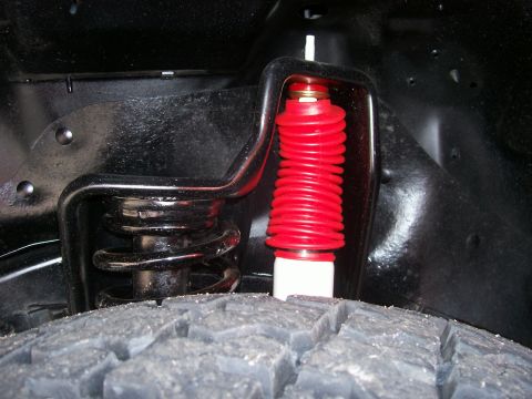 1998 Jeep TJ - A close-up view of a vehicle's suspension system, showing a red shock absorber and black coil spring.
