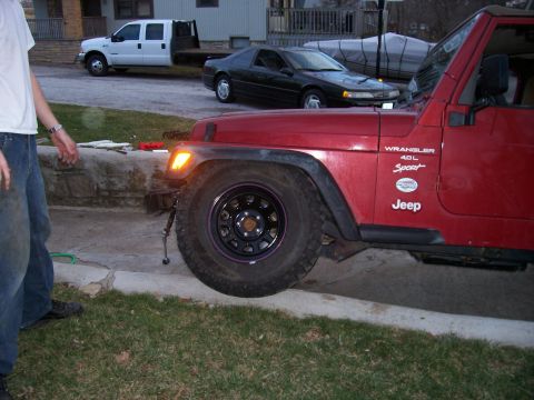 1998 Jeep TJ - A red Jeep Wrangler 4.0L Sport is shown with large tires and aftermarket wheels, parked on a curb.
