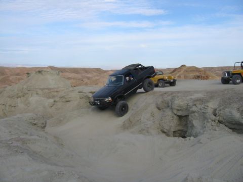 1992 Ford Bronco - A black 1992 Ford Bronco navigates a steep dirt incline in a desert landscape, with two yellow Jeeps visible in the background.