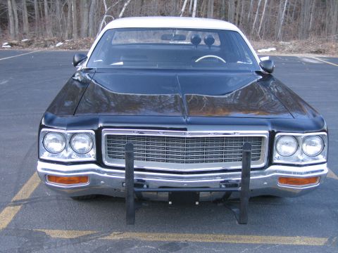 1991 Ford LTD Crown Victoria - Head-on view of a black Dodge sedan with a chrome eggcrate grille reading DODGE, dual round headlights and a black push bar.
