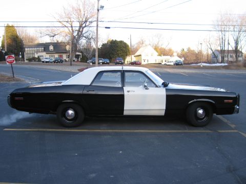 1991 Ford LTD Crown Victoria - Side profile of a long black-and-white four-door police sedan with a white roof and black steel wheels in a parking lot.