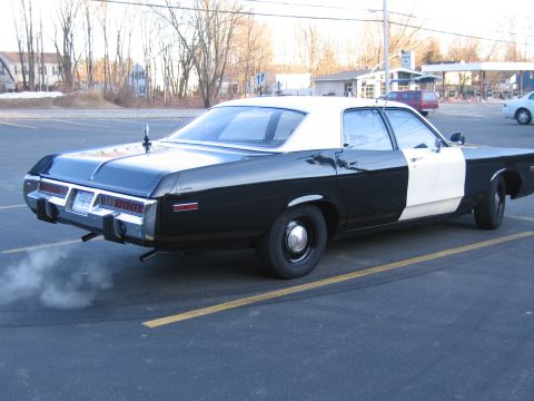 1991 Ford LTD Crown Victoria - Rear three-quarter view of a black-and-white police sedan with rectangular taillights, idling with visible exhaust smoke.