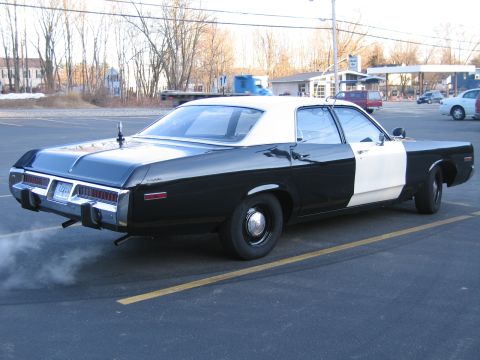 1991 Ford LTD Crown Victoria - Rear three-quarter view of a black-and-white two-door police sedan with a white roof, idling with exhaust smoke in a parking lot.