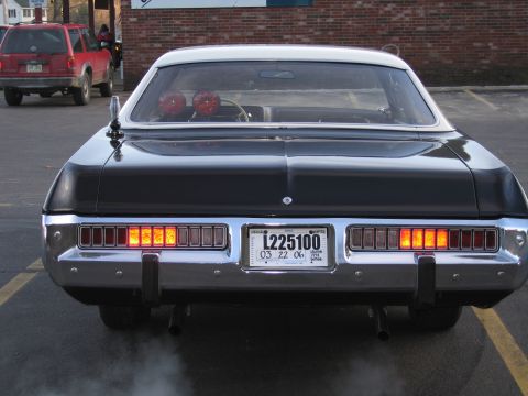 1991 Ford LTD Crown Victoria - Direct rear view of a black police sedan with illuminated rectangular taillights, a red interior light and a plate reading L225100.