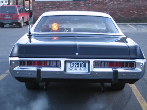 1991 Ford LTD Crown Victoria - Rear view of a black police-style sedan with rectangular taillights and a glowing amber beacon, plate reading L225100.