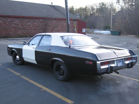 1991 Ford LTD Crown Victoria - Driver-side rear three-quarter view of a black-and-white police sedan with black steel wheels, idling with exhaust smoke.