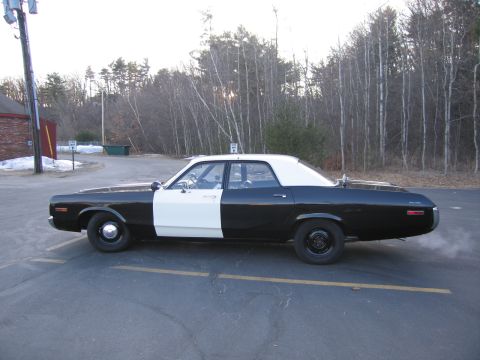 1991 Ford LTD Crown Victoria - Full side profile of a black-and-white four-door police sedan with white roof and door, parked in a lot with bare trees behind.