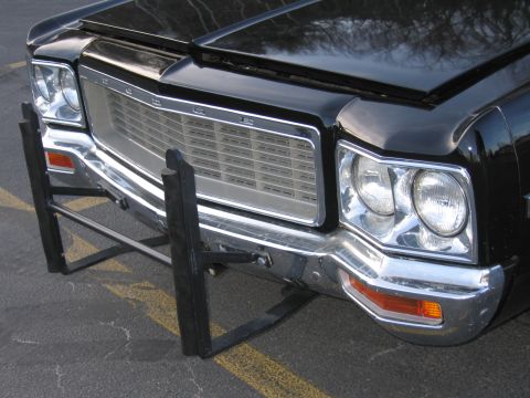 1991 Ford LTD Crown Victoria - Close-up of a black Dodge sedan front showing the chrome eggcrate grille reading DODGE, dual headlights and black push bar.
