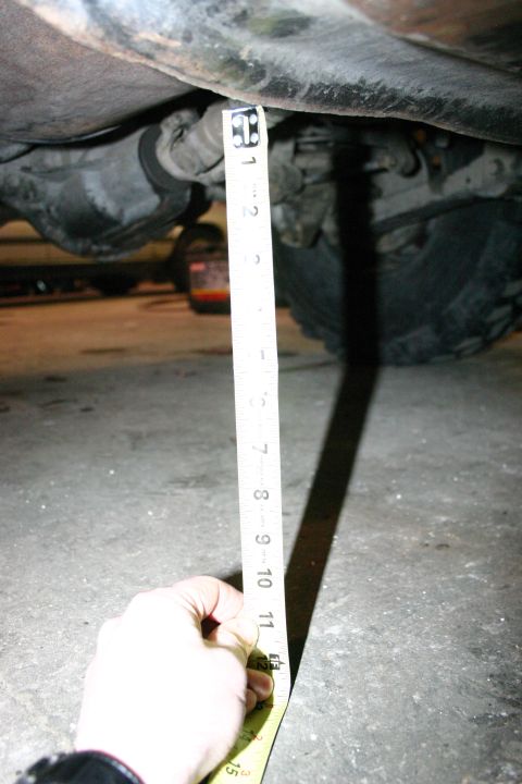 2003 Jeep TJ - A tape measure is used to gauge the clearance under the vehicle's undercarriage, indicating roughly 11 inches.