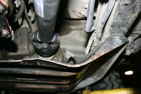 2003 Jeep TJ - Close-up of vehicle undercarriage components, including a driveshaft and a damaged metal plate.