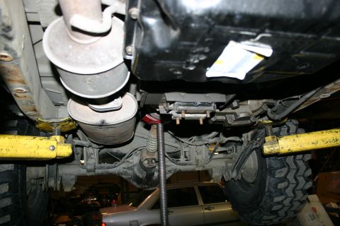 2003 Jeep TJ - The underside of a vehicle is shown, its exhaust pipes and suspension components, with another car in the background.