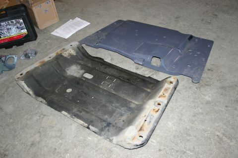 2003 Jeep TJ - Two skid plates, one dark gray and one black, are shown on a concrete floor next to a toolbox and some papers.