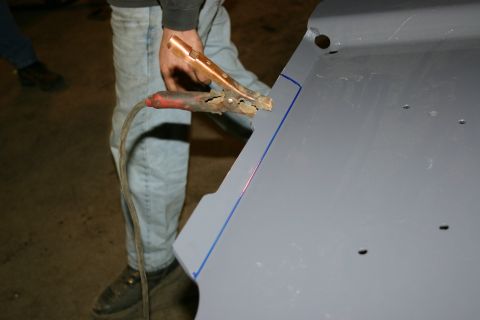 2003 Jeep TJ - A person is welding a gray metal panel, with a welding clamp attached to the surface.