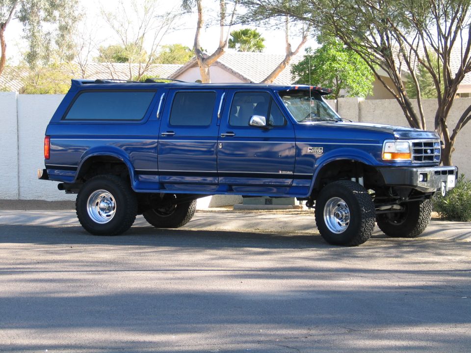 Blue lifted Ford crew cab pickup with matching camper shell on chrome wheels