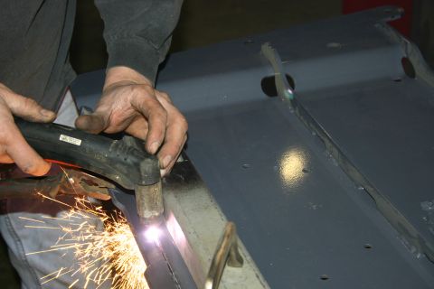 2003 Jeep TJ - A worker uses a plasma cutter to shape a piece of metal, creating a shower of sparks.