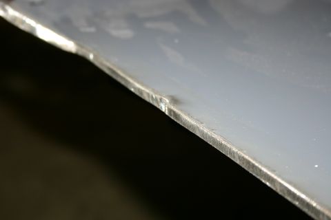 2003 Jeep TJ - The edge of a metal panel shows signs of bending and machining, with a dark background.