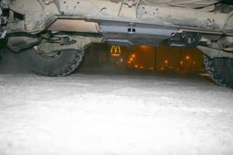 2003 Jeep TJ - The underside of a vehicle is shown, a skid plate and tires, with a McDonald's sign illuminated in the foggy background.