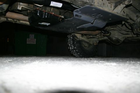 2003 Jeep TJ - Vehicle underbody with skid plate and tire, with a dumpster in the background.