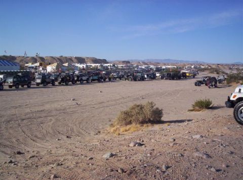 1987 Suzuki Samurai - A large gathering of off-road vehicles are parked in a desert landscape under a clear blue sky.