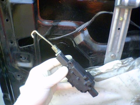 1994 Ford Bronco - A hand holds a door lock actuator inside a vehicle's door panel.