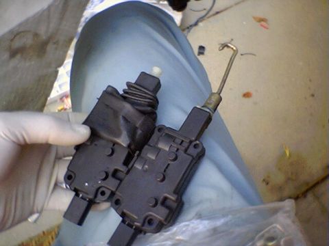 1994 Ford Bronco - Two door lock actuators are held by a gloved hand, one a metal rod mechanism.