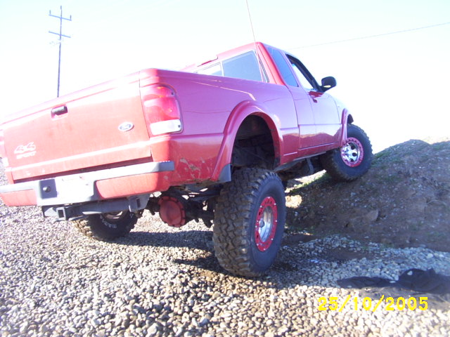 Rear of lifted red Ford Ranger 4x4 flexing over a gravel pile