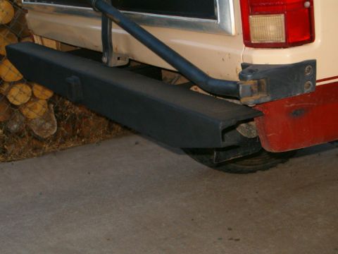 1985 Ford Bronco - The rear of a vehicle shows a black aftermarket bumper and trailer hitch, with a red lower panel.