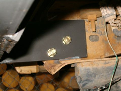 1985 Ford Bronco - A black metal bracket is bolted to a rusty frame, likely part of a vehicle's undercarriage.
