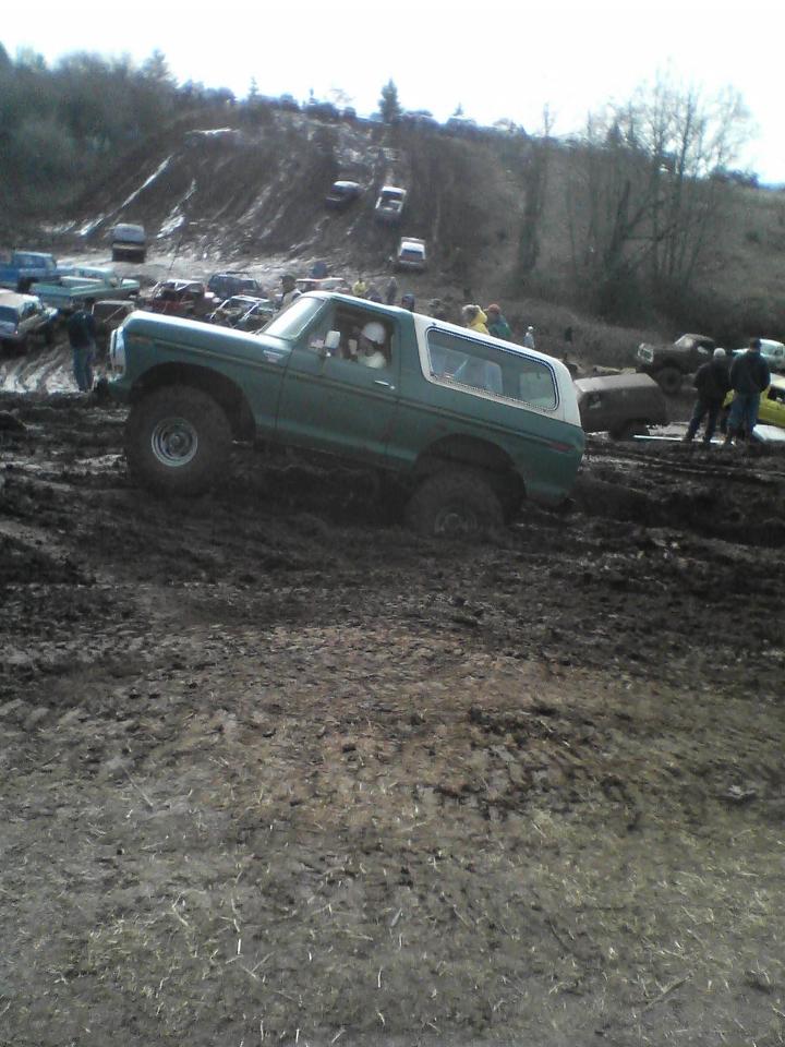 Green 1978 Ford Bronco with white top navigating a muddy hill
