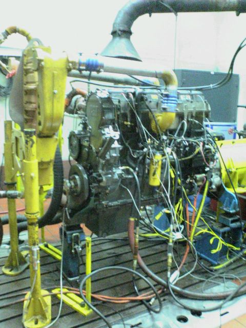1986 Ford Bronco - Engine undergoing testing on a dynamometer, connected to exhaust and fuel lines.