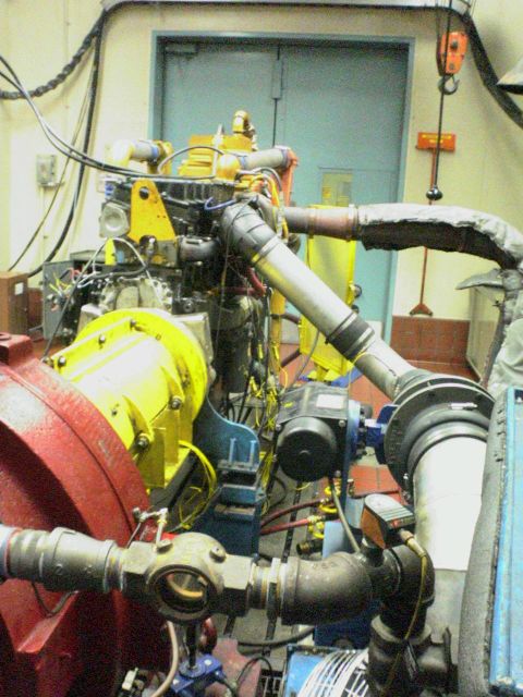1986 Ford Bronco - An engine is mounted on a test stand, yellow and red components and a complex network of pipes and wiring.