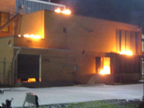 1990 Ford Bronco - yellow building burns at night with flames at the rooftop, upper windows and a glowing doorway.