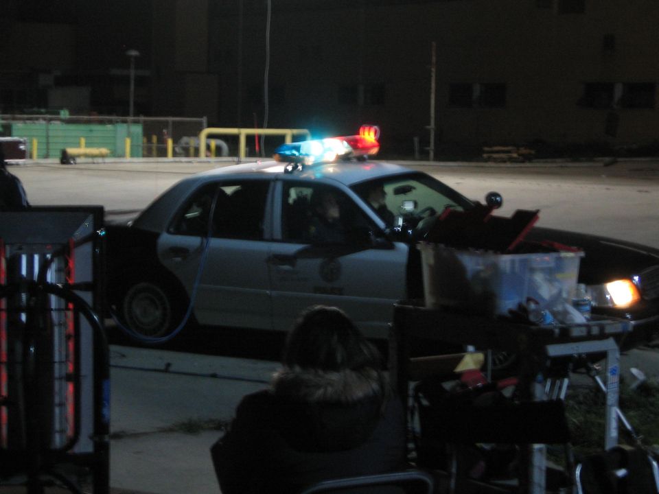 Police car with lights on at night beside film-set equipment