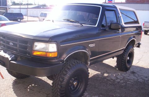 1993 Ford Bronco - This lifted Ford Bronco is parked outdoors on a paved surface, with other vehicles and buildings in the background.
