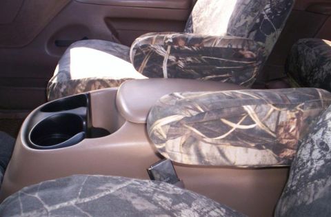 1993 Ford Bronco - The interior of a vehicle shows camouflage seat covers and a tan center console with cup holders.