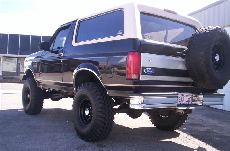 Black Ford Bronco with tan top, lifted with large tires, spare tire on back. License plate 653 JXC