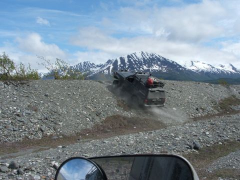1990 Chevrolet Suburban - SUV navigates a challenging gravel incline under a cloudy sky with mountains in the distance.