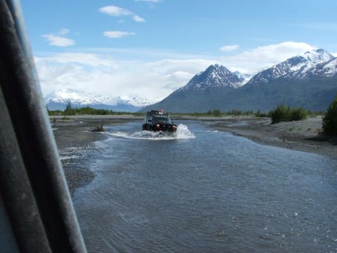 1990 Chevrolet Suburban - An SUV navigates a water crossing in a scenic, mountainous landscape.