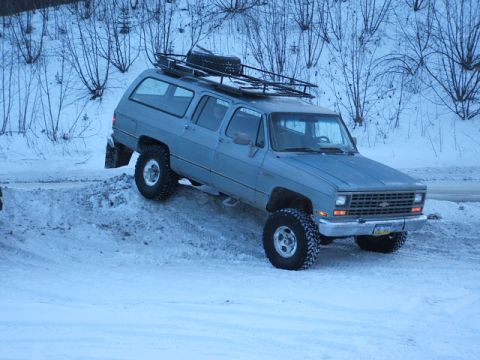 1990 Chevrolet Suburban - A blue 1990 Chevrolet Suburban equipped with a roof rack navigates a snowy incline.