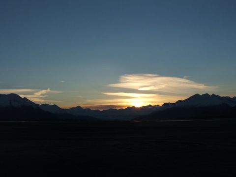 1990 Chevrolet Suburban - The sun sets behind a range of snow-capped mountains, casting a warm glow across the sky.