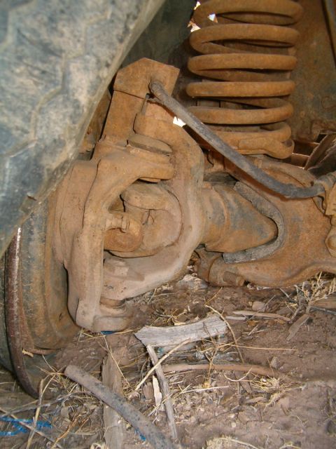 1985 Ford Bronco - Close-up view of the front axle and suspension components, including a rusty coil spring.