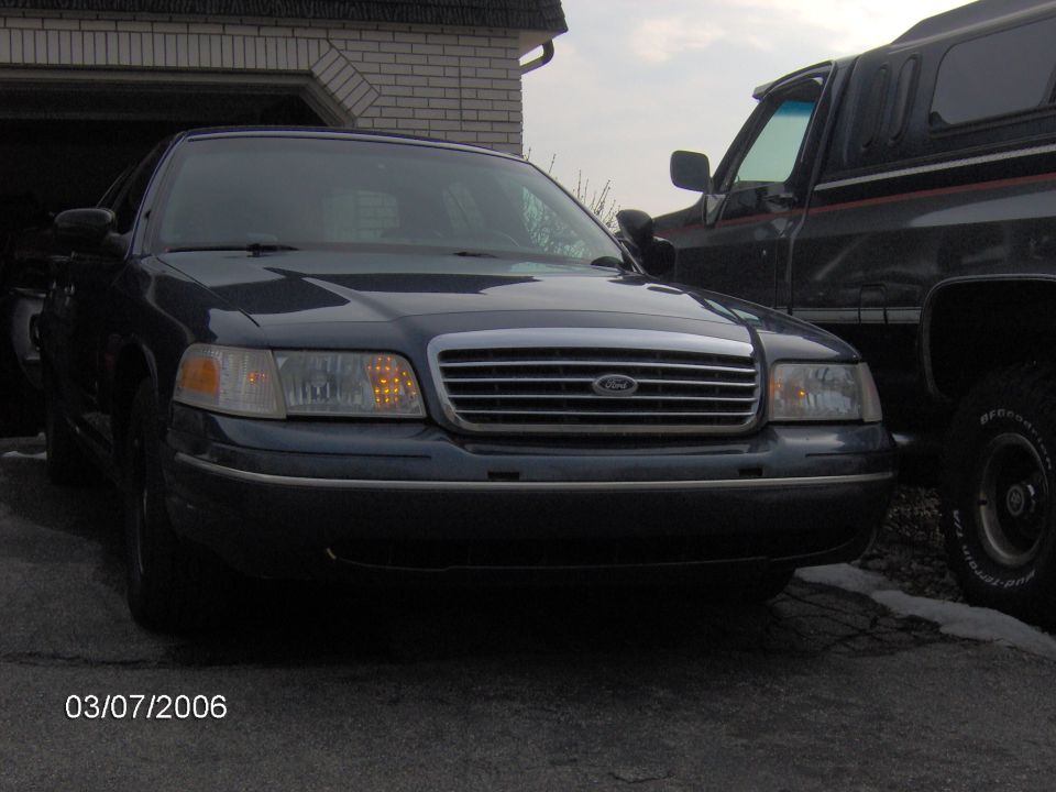 Dark Ford Crown Victoria parked in a driveway beside a black SUV