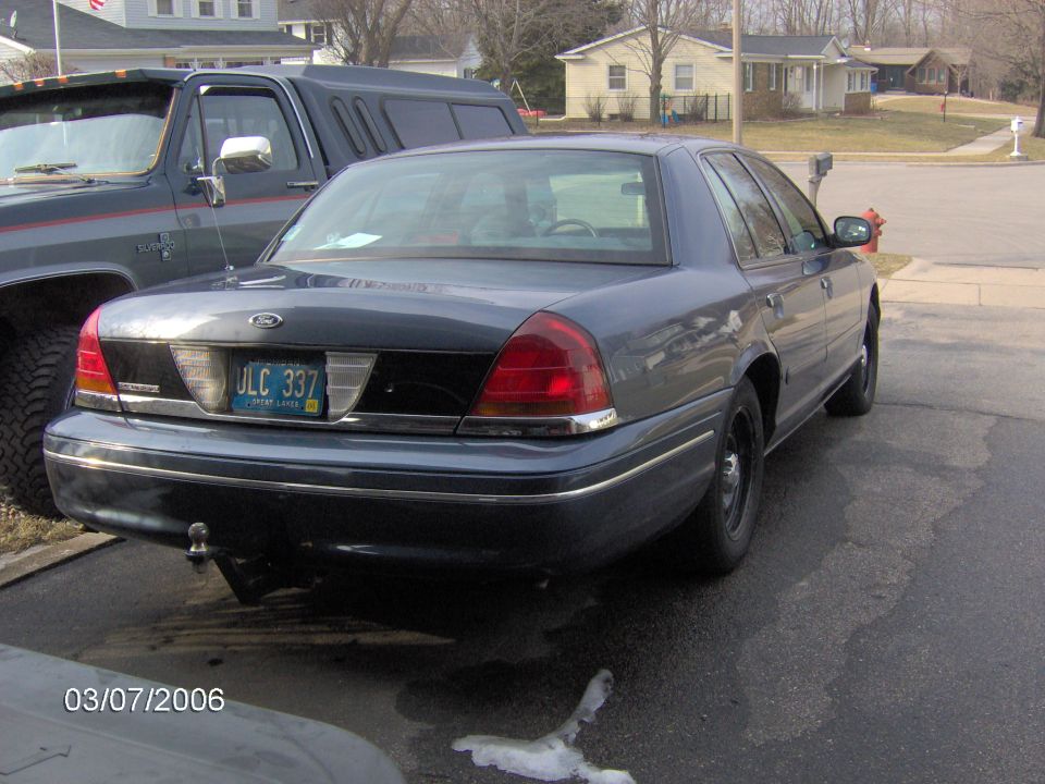 Dark gray Ford Crown Victoria sedan rear three-quarter, parked at curb in suburban neighborhood