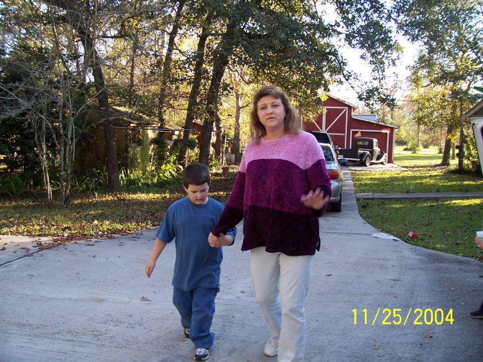 Woman and child walk on driveway near red barn with two vehicles